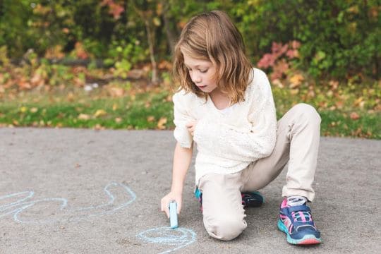 petite fille accroupie qui dessine sur le sol avec de la craie pendant un babysitting à Paris 16