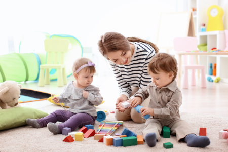 une babysitter jouant avec deux enfants assis par terre pendant son job étudiant