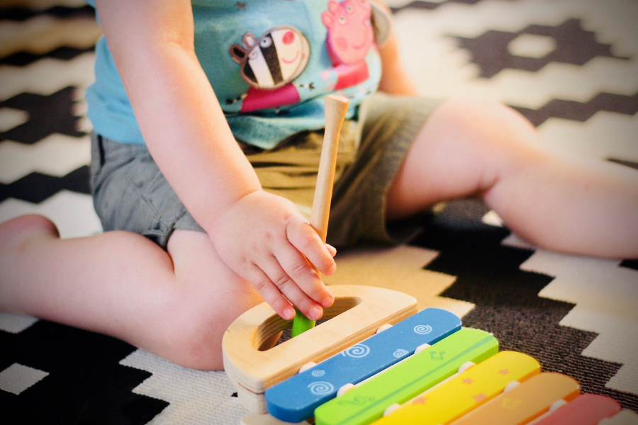 un jeun enfant assis par terre avec un jouet faisant des sons de musique. Une activité d'éveil musical