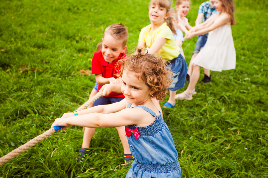 jeu de tire à la corde : les bienfaits du sport. Il y a plusieurs enfants en train de jouer au tire à la corde sur l'herbe