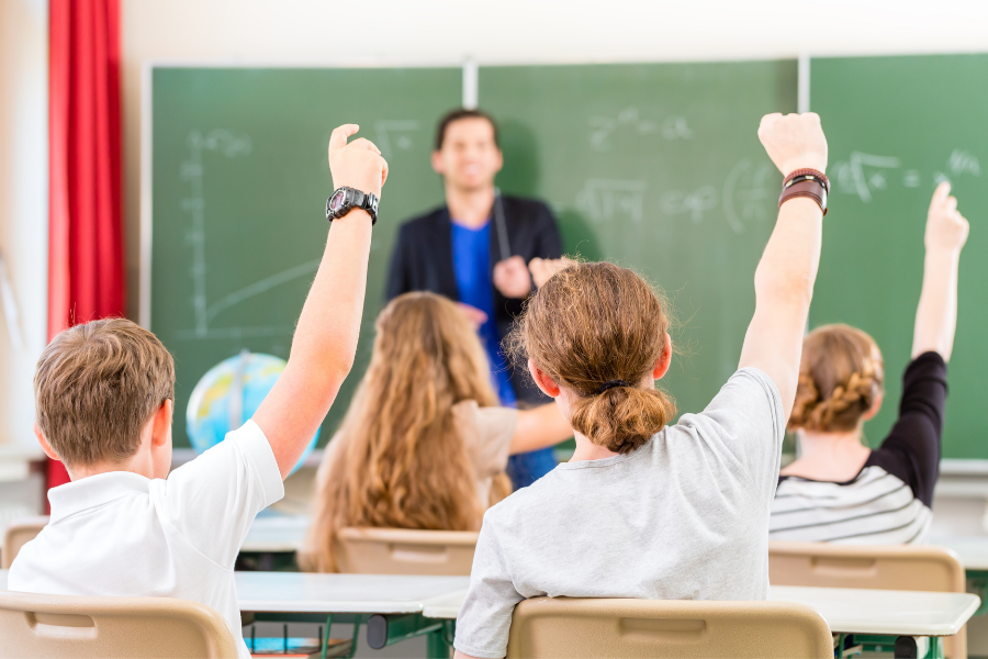 Une classe de 6ème. Le professeur est au tableau et des élèves lèvent la main